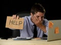 Tired desperate businessman in stress working at office computer desk holding sign asking for help