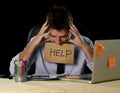 Tired desperate businessman in stress working at office computer desk holding sign asking for help