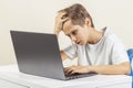 Tired disappointed boy with laptop computer sitting at the table Royalty Free Stock Photo