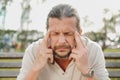 A tired and distressed aged man sits on a park bench. Leans on his hands, rubs his temples. Royalty Free Stock Photo