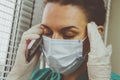 Tired Doctor italian woman in medical mask, gloves and doctor`s suit closed her eyes and talking on a cell phone Royalty Free Stock Photo