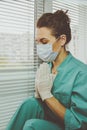 Tired Doctor woman in medical mask, gloves and doctor`s suit closed her eyes, clasped her hands in a gesture of Namaste Royalty Free Stock Photo