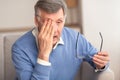 Tired Elderly Man Massaging Eye Sitting On Couch At Home