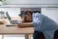 Tired exhausted Asian woman sleeping in kitchen with head on desk near laptop due to addiction Royalty Free Stock Photo