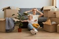 Tired exhausted dark haired woman wearing white t shirt sitting on floor near sofa with her daughter and expressing despair, keeps