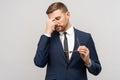 Tired exhausted man, businessman in suit, office worker takes off glasses on grey background.