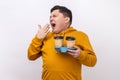 Tired exhausted man holding coffee cups and yawning, feeling bored after stressful working day. Royalty Free Stock Photo