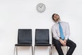 Tired and exhausted man is sitting in waiting room on chair.