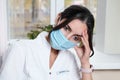 tired exhausted woman doctor wearing medical unform and face mask sitting in front of clinic window and getting rest