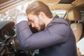 Tired and exhausted young businessman sits on car and leans to steering wheel. He keeps eyes closed. Young man sleeping. Royalty Free Stock Photo