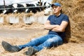 Tired farmer on holiday at a farm among cows sitting on ground