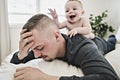 Tired father sleep but his baby boy interferes him. Young happy father lying on bed while his son play with him Royalty Free Stock Photo