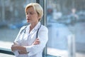 Tired female doctor folding arms, standing next to the window with closed eyes Royalty Free Stock Photo