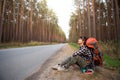 Tired female tourist sits on the side of the road with huge backpack and a mat. Domestic tourism, independent travel alone,