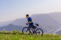 Tired fit mountain biker pushing his bike uphill at the top of the mountain on a sunny day with amazing view on a blue river