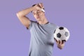 Tired football player with ball wiping sweat after game or championship over lilac studio background