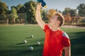 Tired football player pouring water on face. He shrinks. Young man stand on lawn. Four balls are behind him.