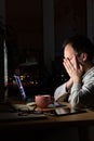 Tired freelancer male rubbing his eyes, sitting at a desktop PC/laptop late at night, falls asleep from fatigue Royalty Free Stock Photo