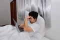 Tired frustrated Asian man with laptop leaning pillow on the bed in bedroom. Overload working concept. Royalty Free Stock Photo