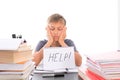 Tired frustrated boy sitting at the table, doing his homework among pile of books. Word Help is written on open notebook Royalty Free Stock Photo