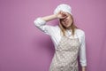 Tired girl cook in apron covers her face with a hand on a pink background, sad housewife in kitchen clothes in stress Royalty Free Stock Photo