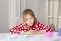 tired girl has her hands folded on school notebook and looks at camera, studying at home at table. child is doing homework. Royalty Free Stock Photo