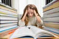 A tired girl with long blond hair holds her head next to a pile of textbooks and an open book. Royalty Free Stock Photo