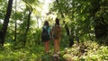 Tired girls travelers with backpacks go through the thicket in the forest. Hiker woman walks in the forest. happy hiker