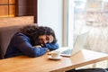 Tired handsome young adult man freelancer in casual style sitting in cafe with laptop, sleeping on the table after hard overtime Royalty Free Stock Photo