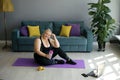 A tired happy fat woman is sitting on a training mat holding a bottle of water in her hand.