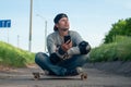 Tired happy young skater dozing sitting on a skateboard, breathing fresh air. People and the concept of relaxation, Royalty Free Stock Photo