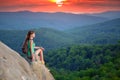 Tired hiker girl relaxing on rocky mountain top enjoying evening nature during travelling on wilderness trail. Lonely Royalty Free Stock Photo