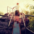 Tired hiker keep handrail on peak. Sunny spring daybreak in rocky mountains. Hiker with red baseball cap, dark pants and white shi Royalty Free Stock Photo