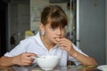 Tired hungry schoolgirl eating soup at the table in the kitchen