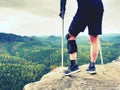 Tired hurt tourist with medicine crutches. Man with broken leg in knee brace features resting on exposed rocky summit