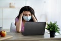 Tired Indian teen girl in face mask suffering from headache in front of laptop at home