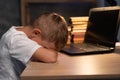 Tired kid fell asleep next to laptop doing school homework at night, closeup. Exhausted boy student sleeping on desk in Royalty Free Stock Photo