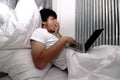 Tired laziness Asian man working on laptop on the bed in bedroom. Royalty Free Stock Photo