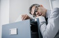 Tired lazy office worker leaning on a filing cabinet and sleeping, he is falling asleep standing up; stress, unproductivity and Royalty Free Stock Photo