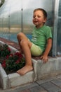 A tired little boy sits on a path near a bed barefoot. farmer boy children