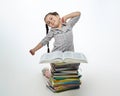 Tired little girl sits in front of a large stack of books and stretches