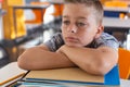 Tired looking caucasian schoolboy sitting at desk in classroom leaning on a pile of schoolbooks Royalty Free Stock Photo