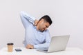 Tired male employee sitting office workplace, touching sore back neck, massaging hurting shoulders