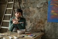 Tired man in an art studio sits on a chair after painting an abstract painting. A modern and successful artist holds a