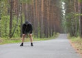 Tired man in grey hoodie making a stop after jogging on road in the forest, selective focus