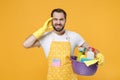 Tired man househusband in apron rubber gloves hold basin with detergent bottles washing cleansers doing housework