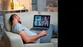 Tired man in pajamas sitting on sofa falling asleep while having online business videocall with teammates Royalty Free Stock Photo