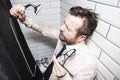 Tired man in a shirt and tie closed his eyes and leaned against the wall in the bathroom, holding glasses in one hand, and in the Royalty Free Stock Photo