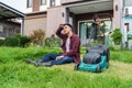 Tired man sitting with law mower for cutting grass at home Royalty Free Stock Photo