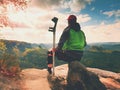 Tired man tourist sit with hurt knee in immobilizer or rock, hold medicine pole. Open forest landscape